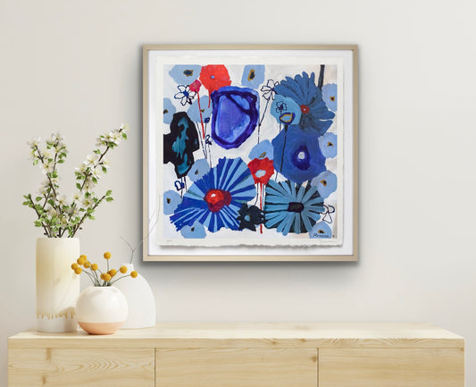 Framed abstract art with blue and red flowers on a wall above a wooden console table.