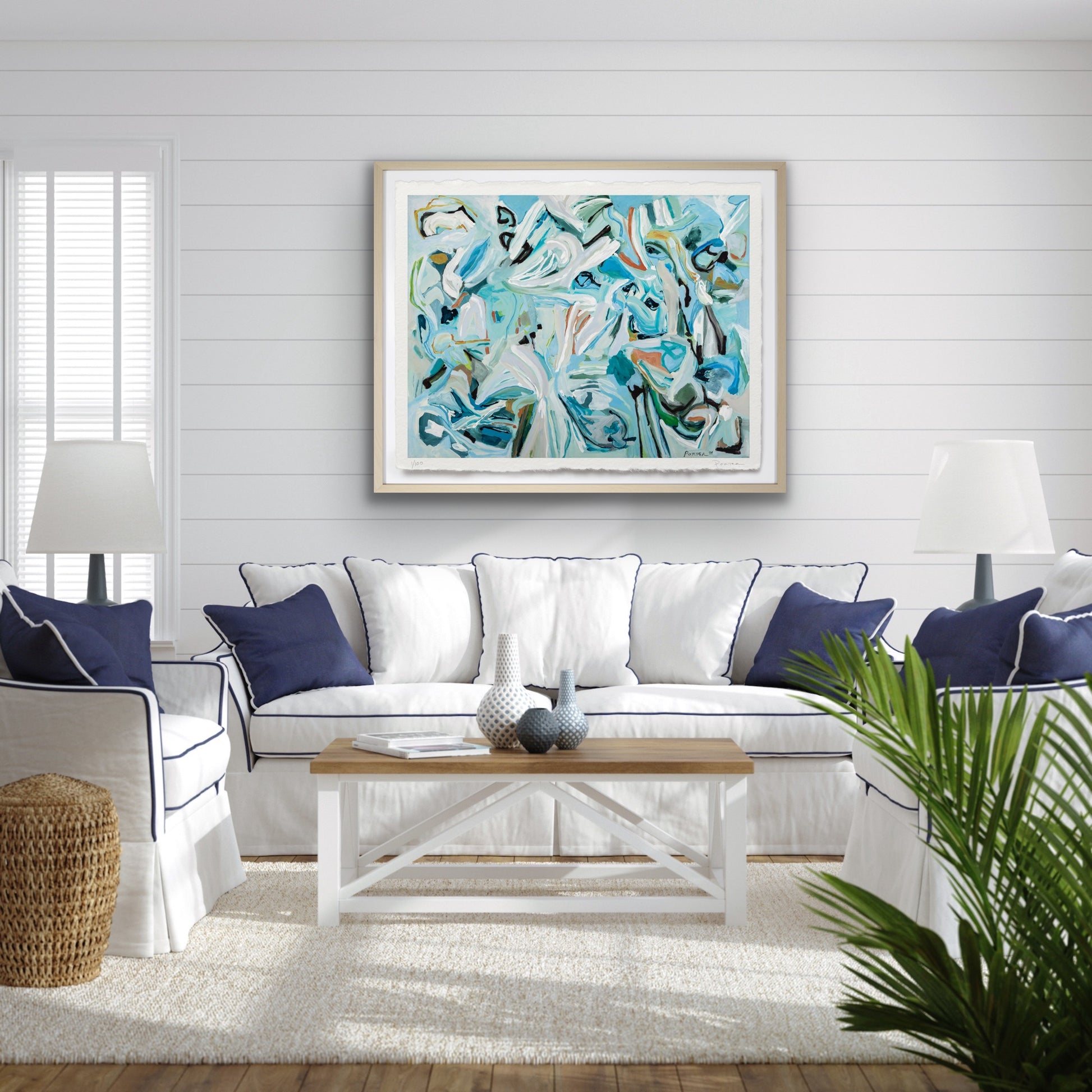 Living room with a white sofa, blue pillows, a wooden coffee table, and a colorful abstract painting on the wall.
