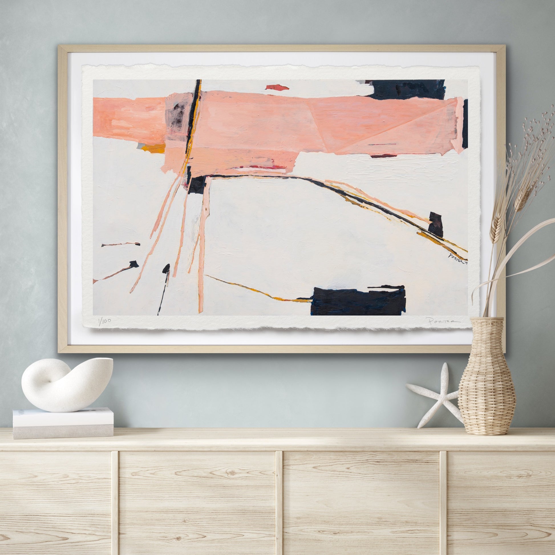 Abstract pink and gold painting on a wall above a wooden cabinet with decorative items.