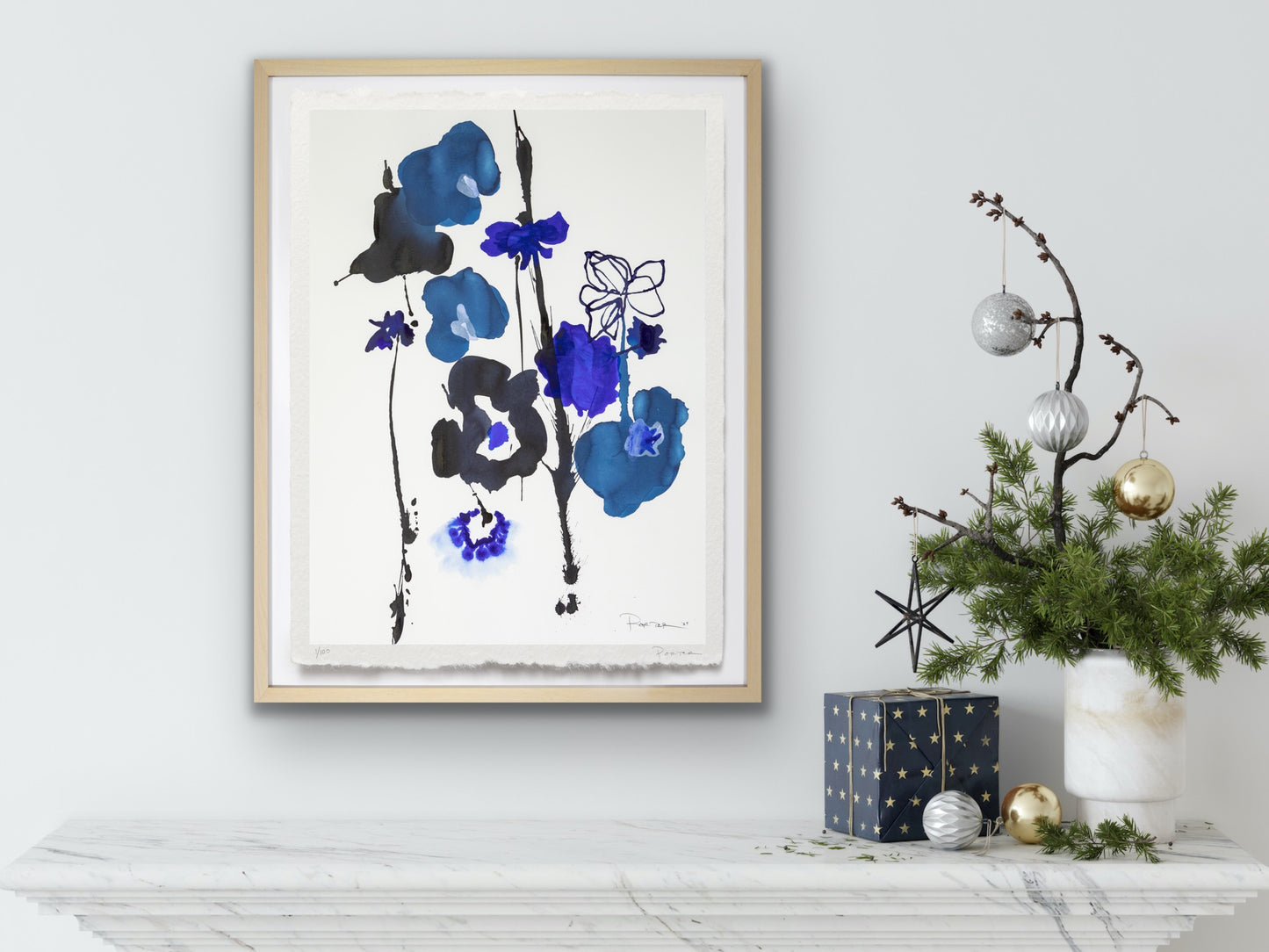 Framed floral  abstract artwork with blue and black flowers on a white wall, next to Christmas decorations.