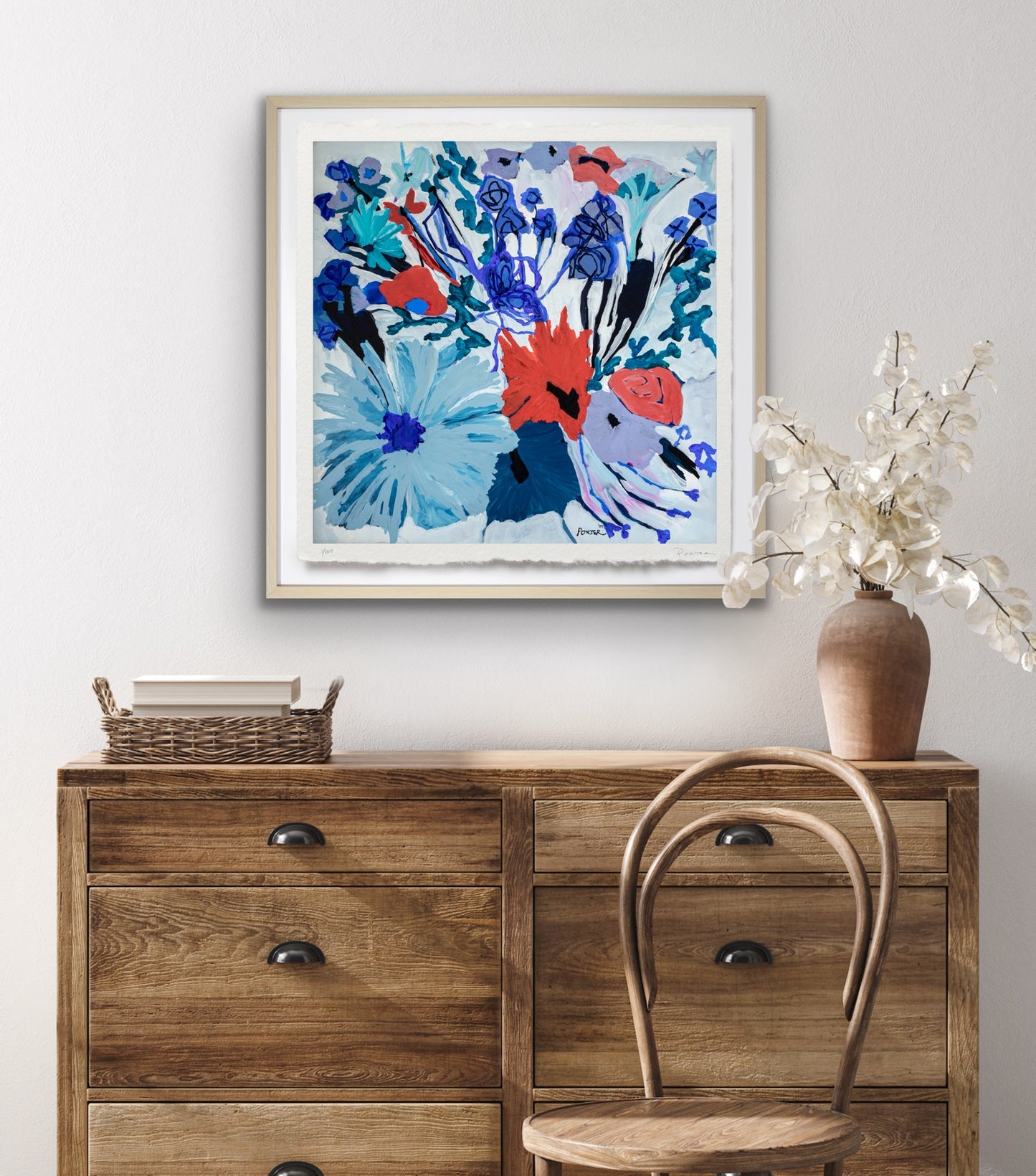 Framed abstract artwork on a wall above a wooden dresser with a chair and vase.