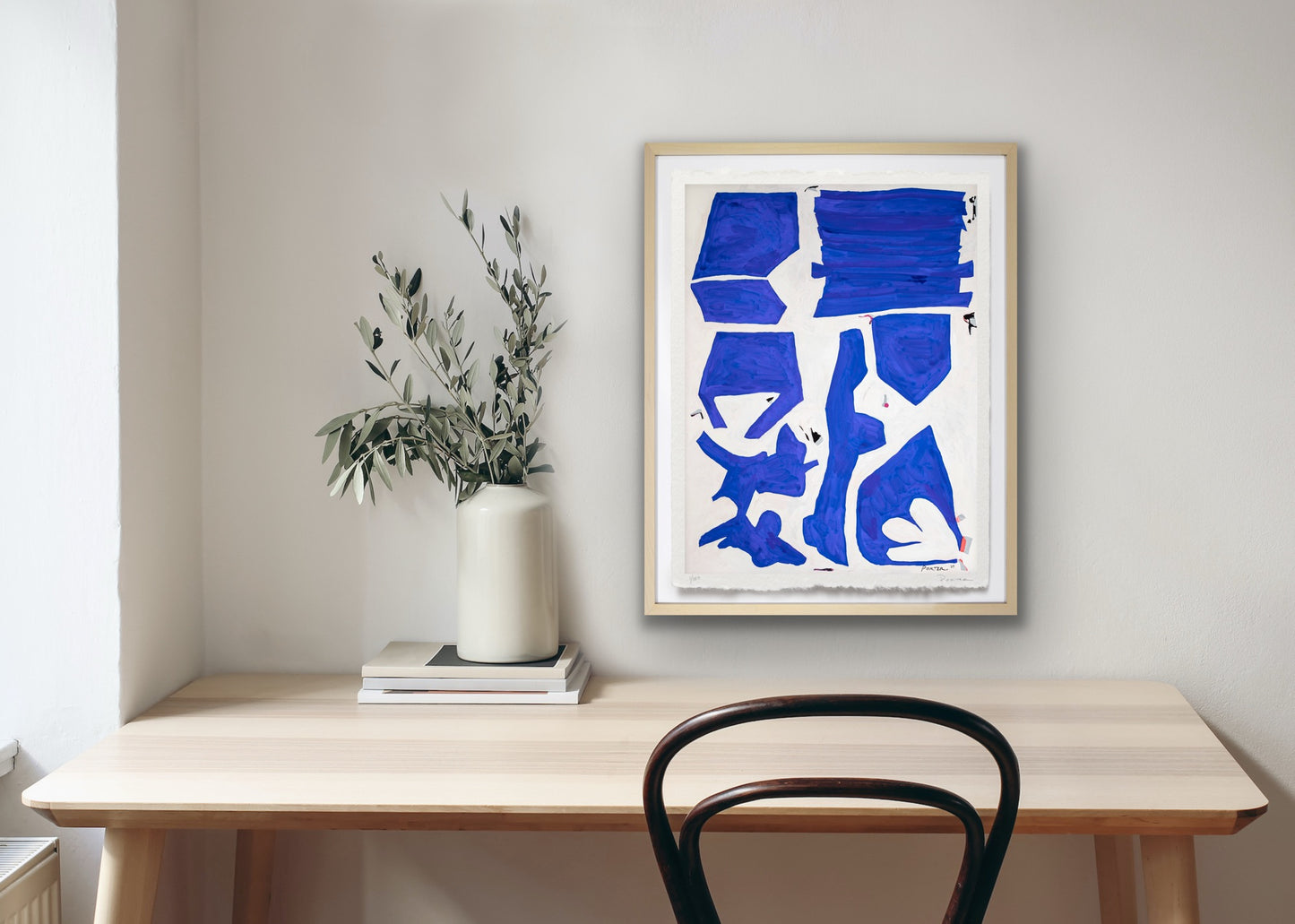 Framed blue and white geometric abstract art on a wall above a wooden desk with a chair.